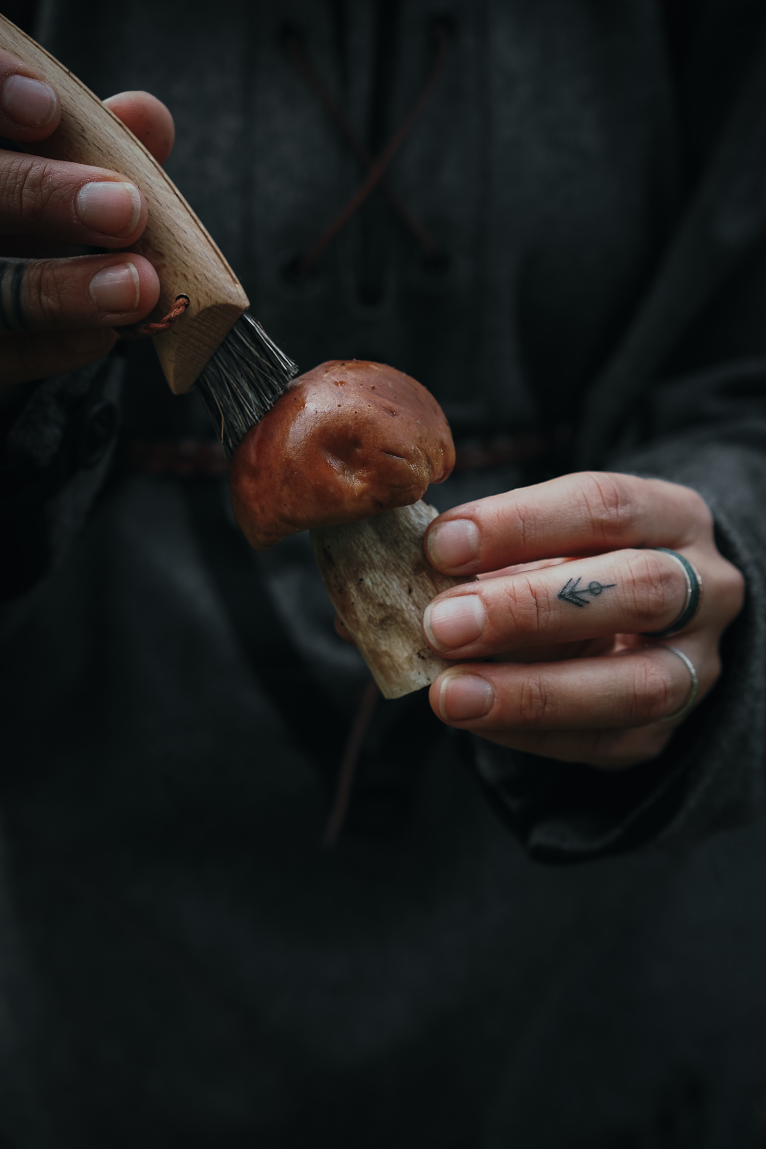 tattooed hands cleaning a bolete mushroom