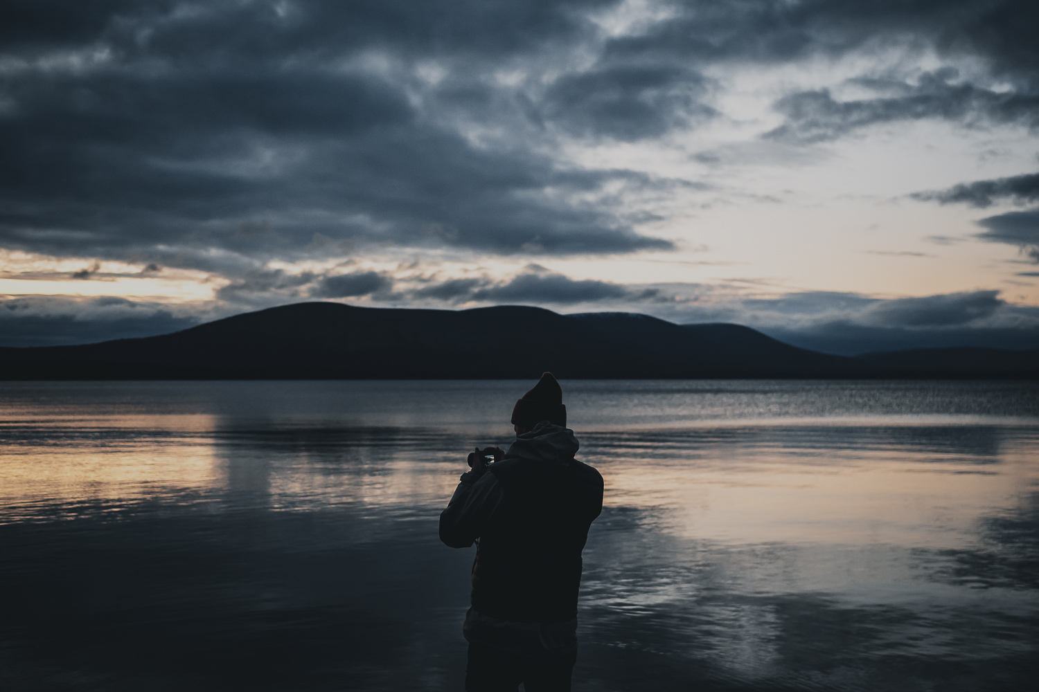 man taking a photo of the sunset by a lake